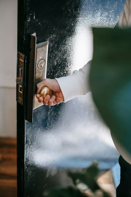 High angle of crop unrecognizable person holding round shaped handle while opening door at home