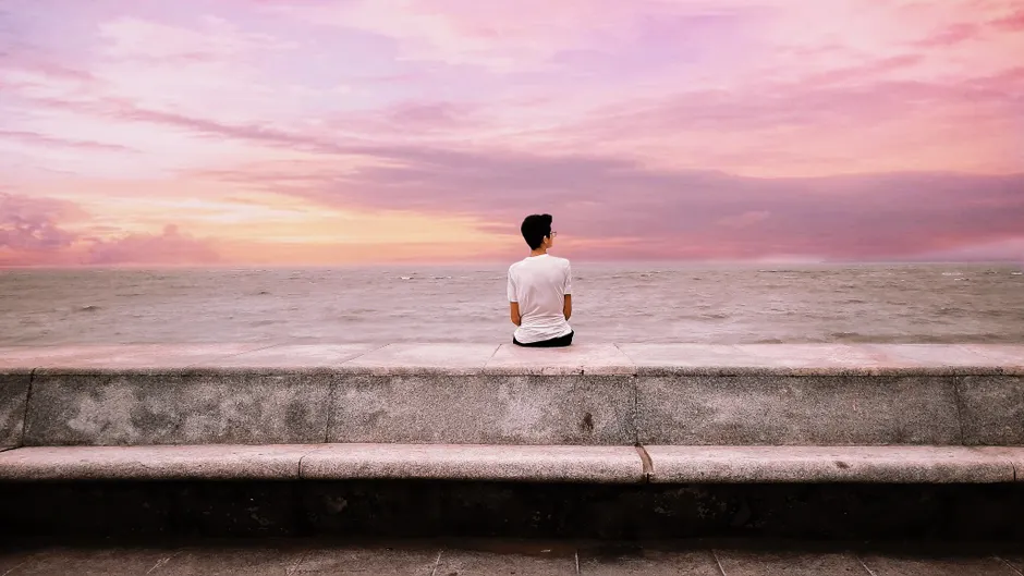 Man sitting alone by the ocean at sunset, embracing peace and tranquility.