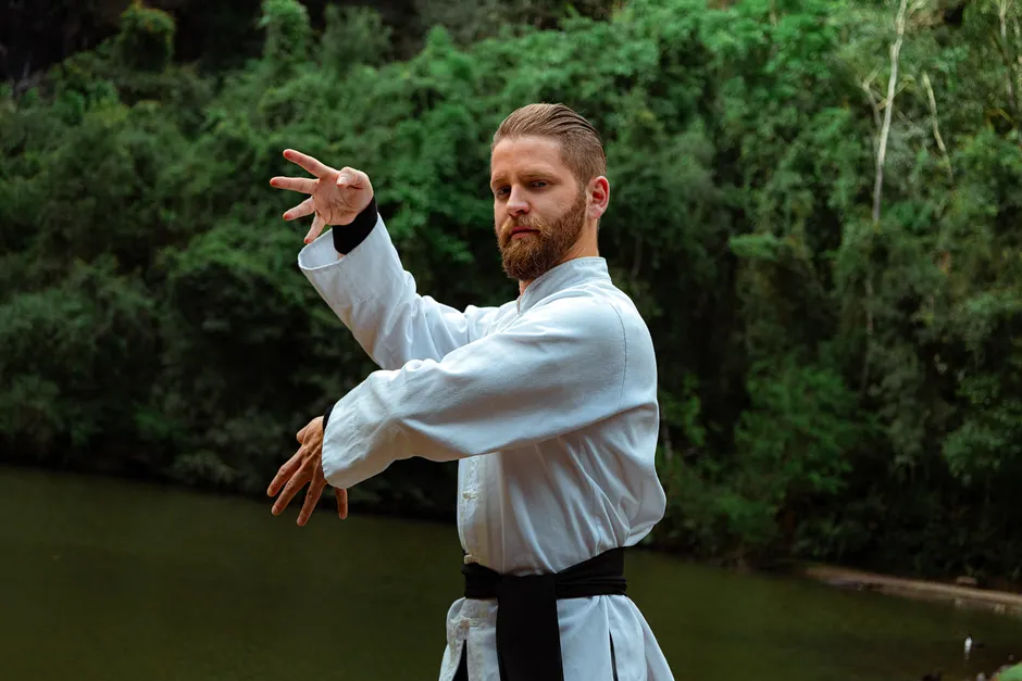 Martial artist in karate uniform practicing outdoors by a serene water body.