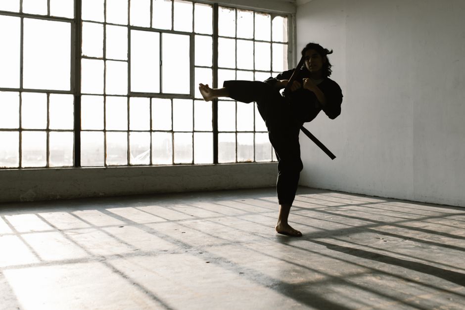 Martial artist in silhouette practicing a high kick in an industrial studio space.
