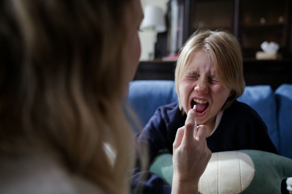 Probiotiques et autisme en 2026 : état des preuves Mother administering medicine to a sick child holding mouth open on a couch indoors.