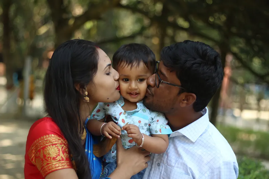 Parents kiss their smiling child in a Joyful outdoor family portrait in Bangladesh.