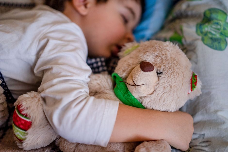 Peaceful sleeping child hugging a teddy bear in bed for comfort and warmth.