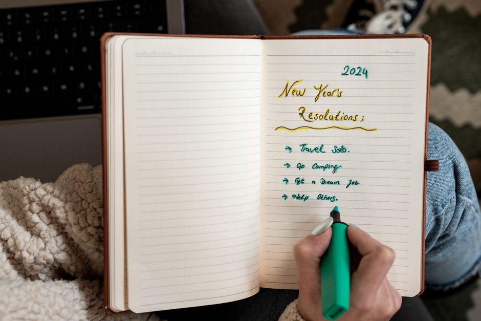 Person making 2024 New Year's resolutions in a notebook with a green marker.