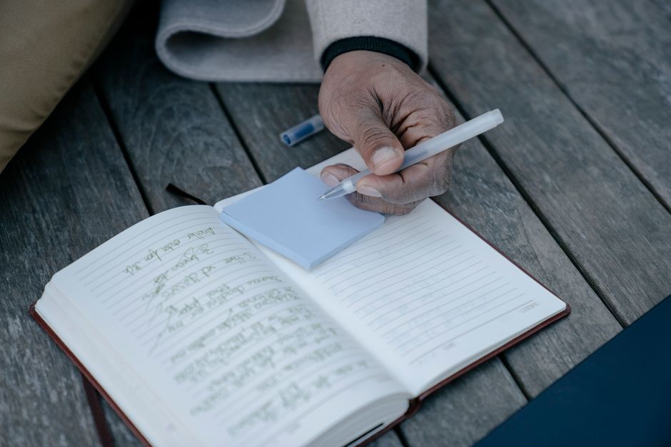Person writing in a journal, focusing on hand holding pen with notepad on a wooden table.