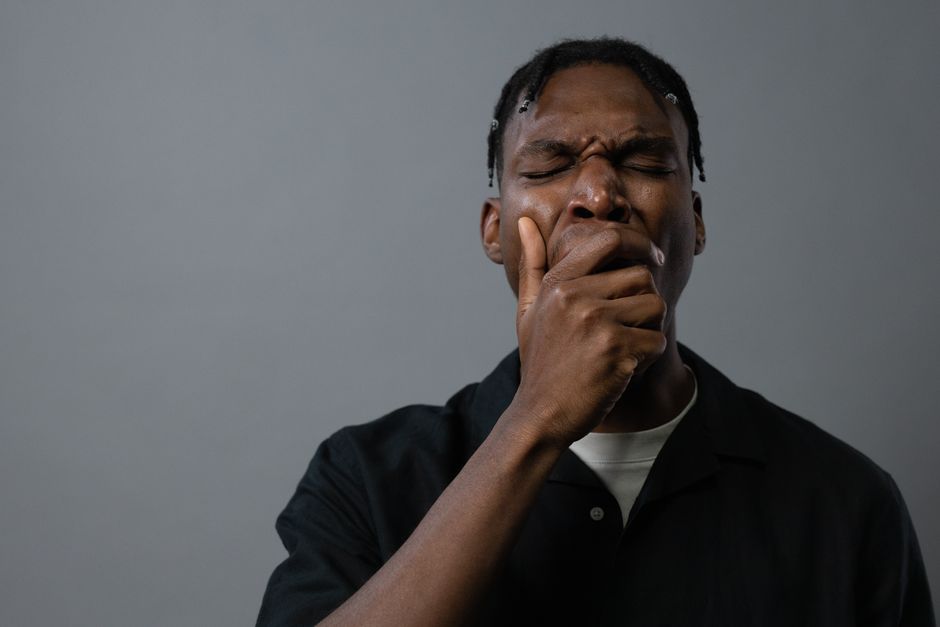 Bâillements excessifs : quand ce réflexe banal mérite un avis médical Portrait of a tired man yawning with hand on mouth, showing fatigue and exhaustion.
