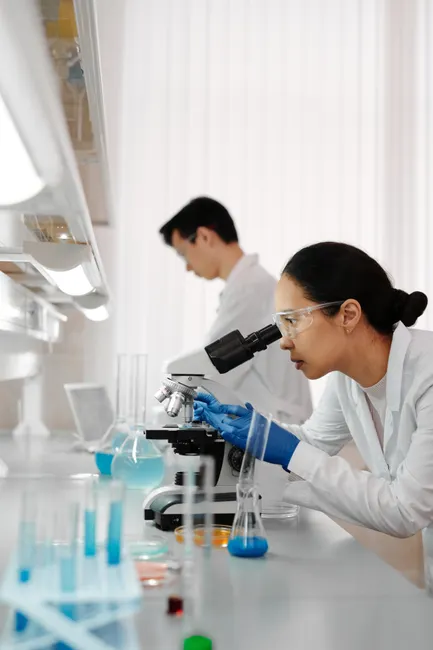 Researchers in a lab analyzing samples using microscopes and glassware.