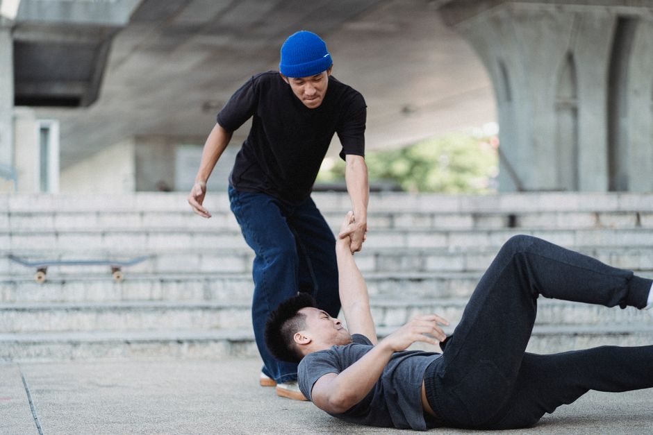Serious ethnic male in casual clothes helping injured friend while training on street near stone stairs