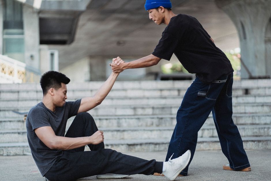 Aider les autres rend-il plus heureux? Ce que montrent quatre études Side view Asian man in street wear holding friends hand and helping to get up from ground on sunny street