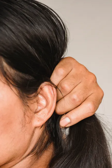 Side view of crop anonymous ethnic person with pure skin touching smooth hair on light background