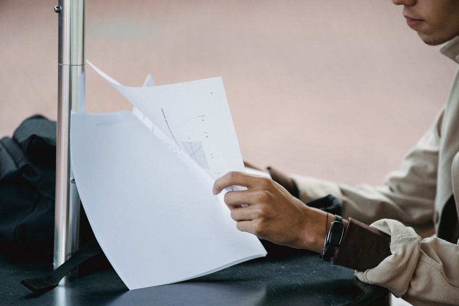 Side view of crop anonymous learner reading papers with test while studying alone