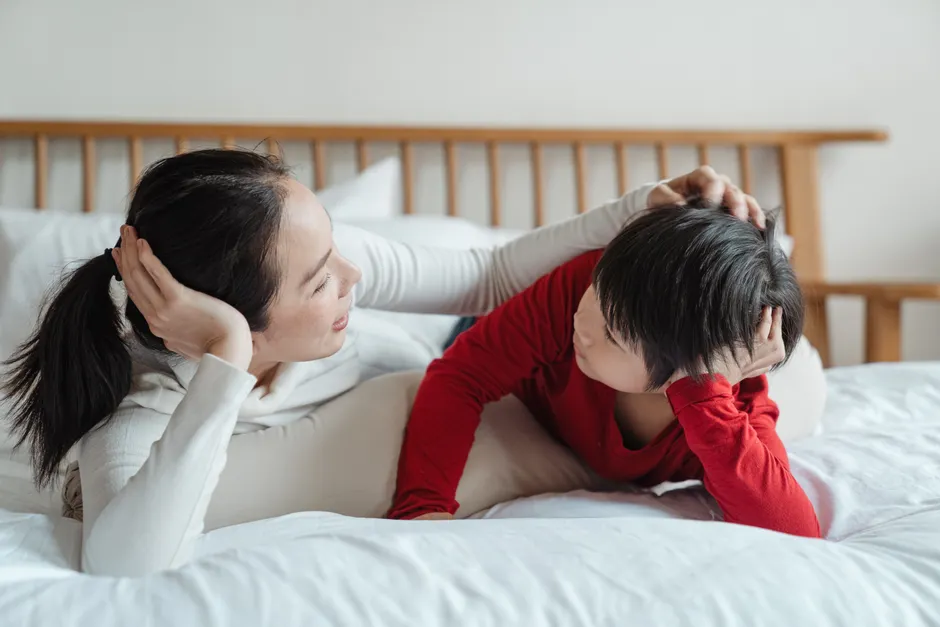 Dépression parentale : tenir le lien sans jouer au parent parfait Side view of full body mother and little son in casual outfit lying on bellies together on bed leaning heads on hands while mother patting child on head during talking