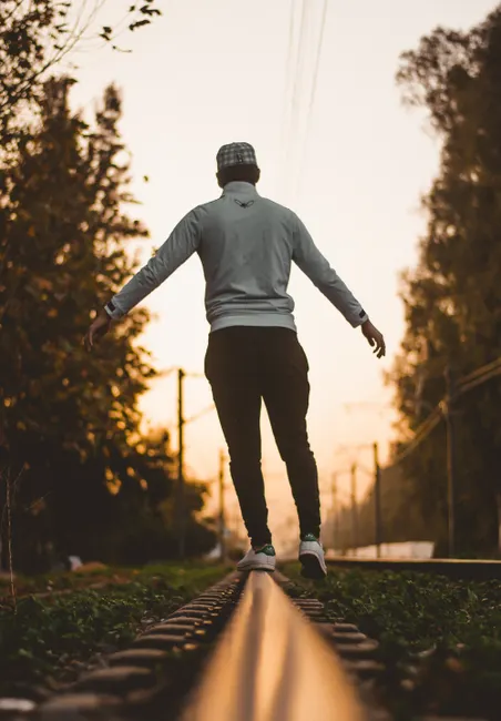 Silhouette of a man balancing on railroad tracks at sunset, conveying adventure and freedom.