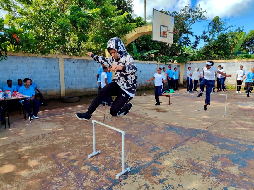 Students participating in a sports activity, jumping hurdles outdoors on a sunny day.