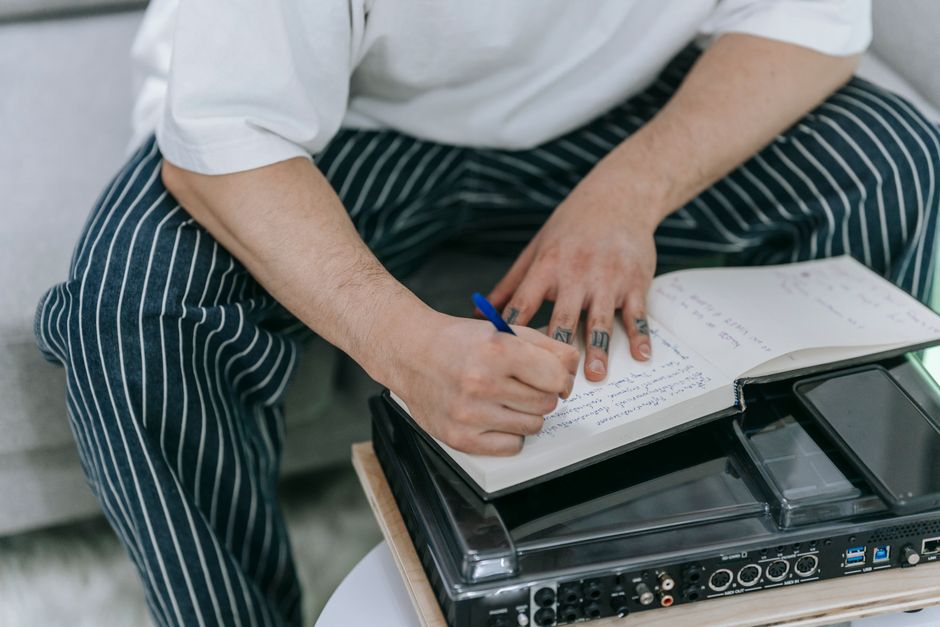 Tattooed individual writing in a notebook indoors, focusing on creativity and expression.