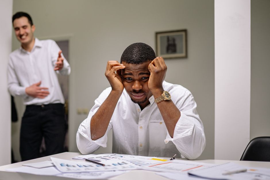 Stress chronique : ce qu’il change dans le corps et comment agir Tensed businessman at desk while coworker is laughing. Office stress concept.