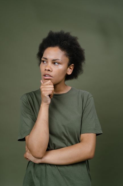 Thoughtful person with afro hair in green shirt looking pensive against a plain background.