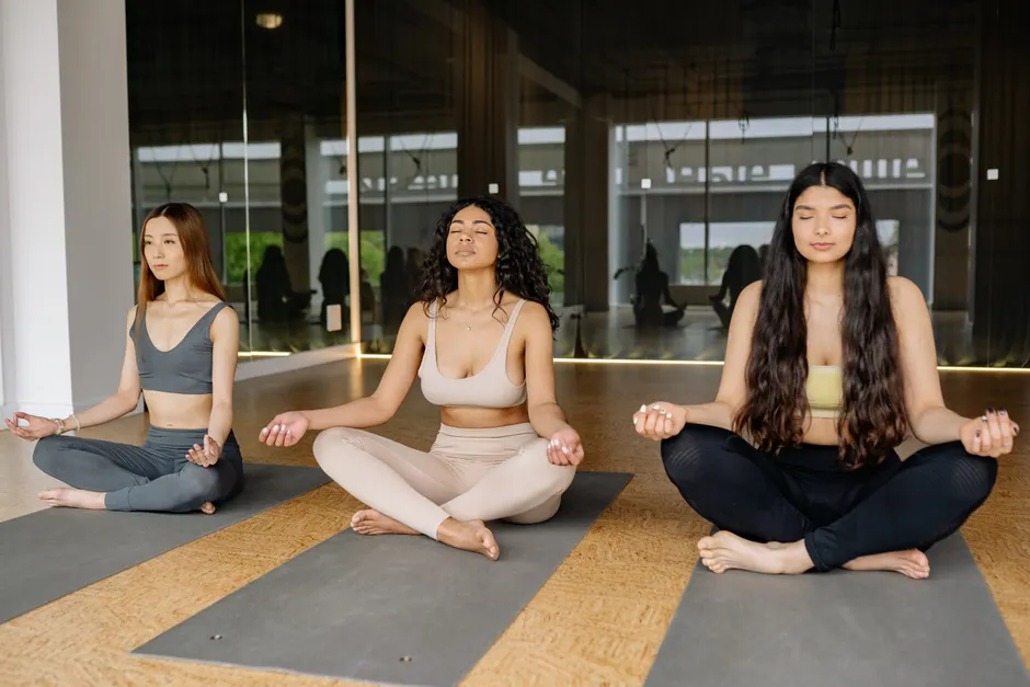 Three women practicing meditation in a yoga class indoors, promoting a calm and healthy lifestyle.