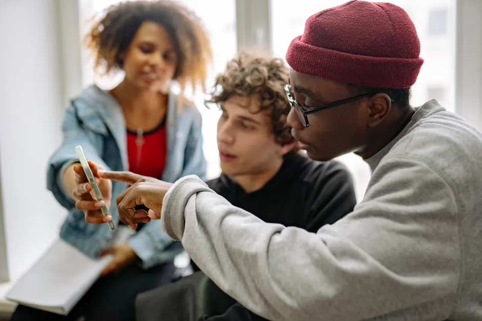 Cancel culture : ce que la psychologie montre sur la validation collective Three young adults discussing content on a smartphone indoors.