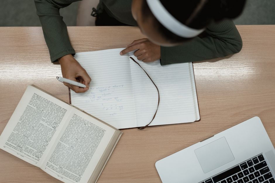 Mémoire didactique : ce que recouvre le terme et comment mieux retenir Top view of a person studying with an open book and laptop, writing notes in a notebook.