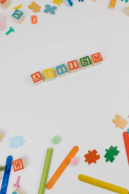Top view of autism awareness concept using wooden blocks, puzzle pieces, and toys on white background.