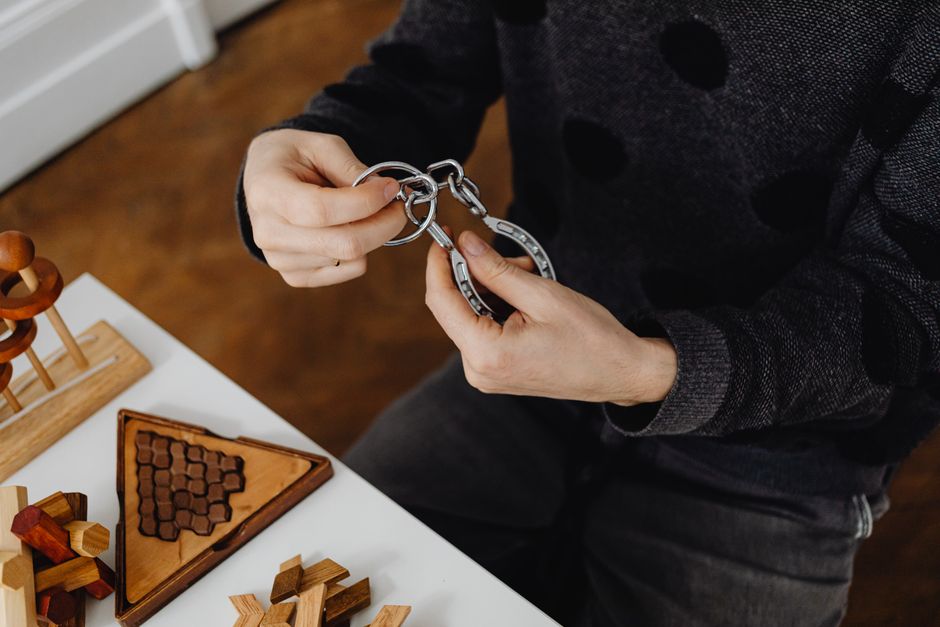 Exercices cérébraux : ce que l’entraînement cognitif améliore vraiment en 2026 Top view of hands solving metal puzzle, surrounded by wooden brain teasers on a table.