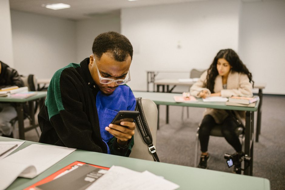 Two college students using smartphones possibly during an exam in a classroom setting.