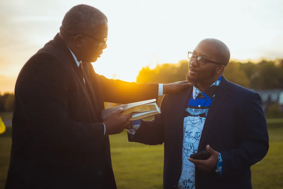 Two men having a meaningful conversation outdoors with an open book during sunset.