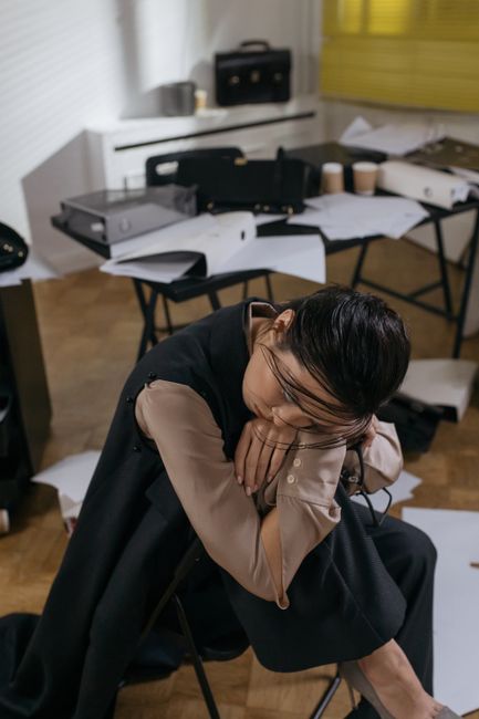 Woman in an office environment, tired and leaning on a desk, surrounded by paperwork.