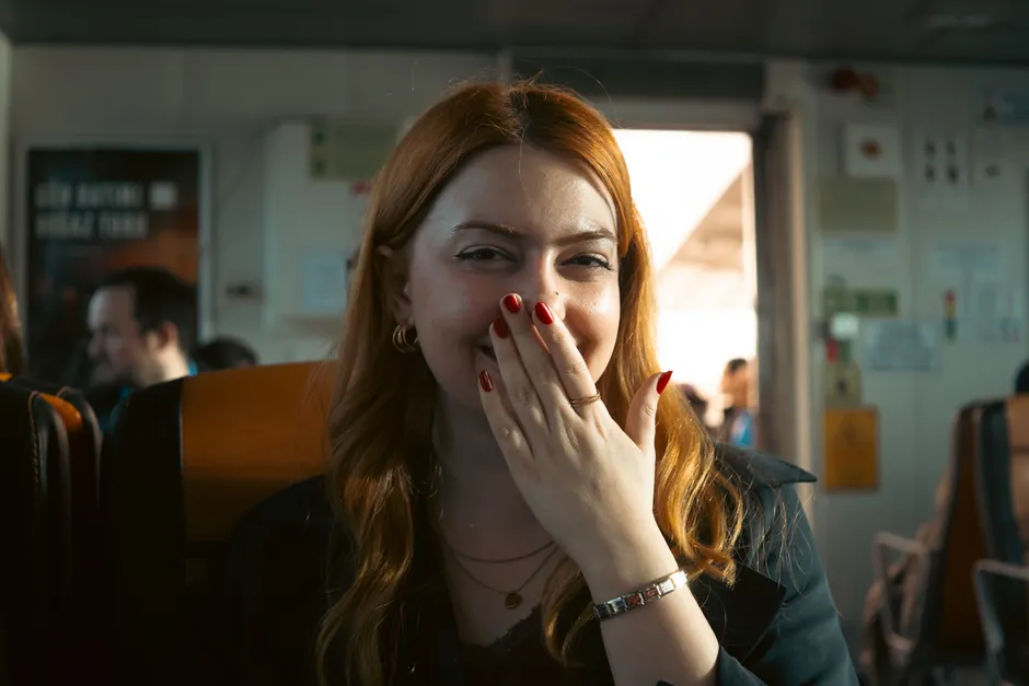 Arrêter de se ronger les ongles : sortir du pilote automatique Woman with red hair and nails smiling indoors, hand over mouth.