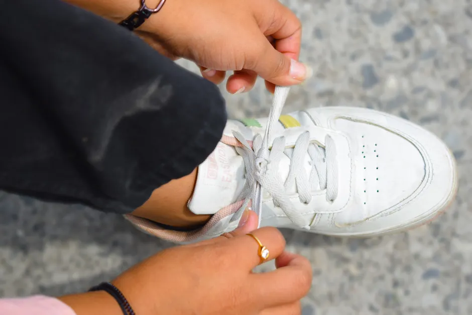 Woman's hands tying shoelaces on a white sneaker outdoors. Casual fashion detail.