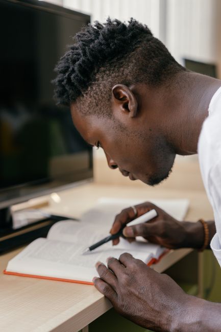 Young African American man studying indoors, focused on reading a book.