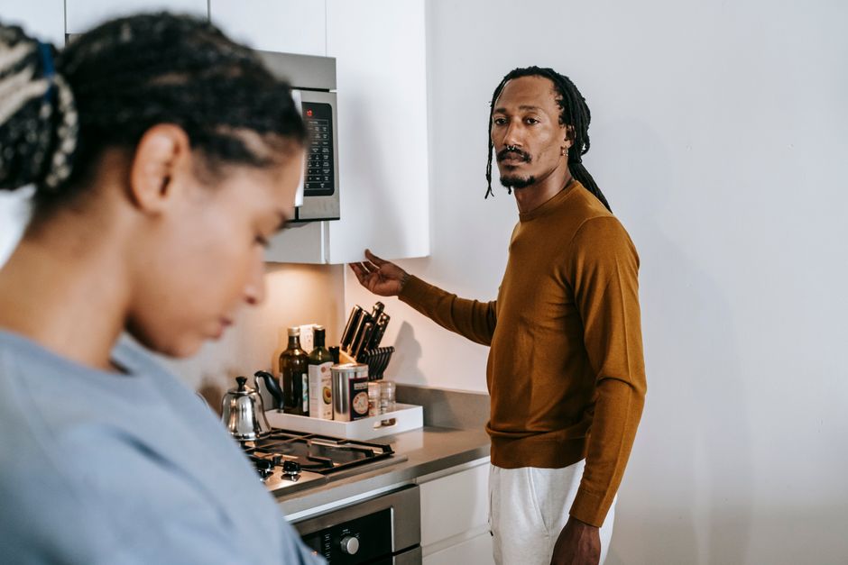 Young black couple in casual outfit standing at kitchen and arguing with each other at home