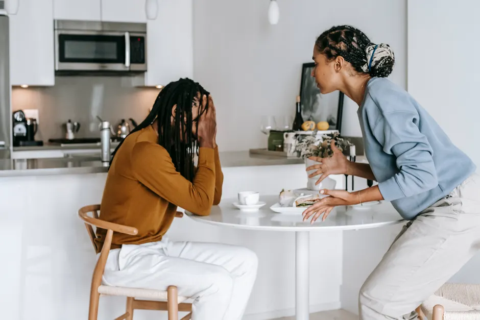 Amour Mania : quand la passion nourrit l’insécurité Young black man sitting at table with hands on head and having conflict with standing near table woman in light kitchen