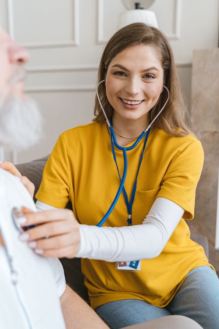 Young female healthcare worker in yellow shirt listens to patient with a stethoscope.
