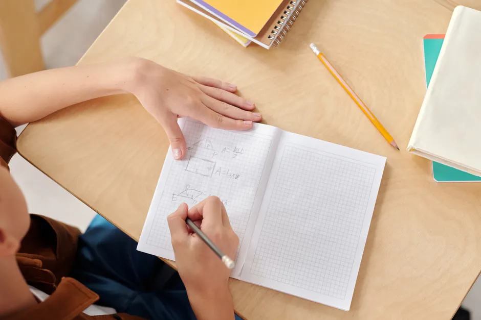 Young student writing math equations in a notebook at school desk.