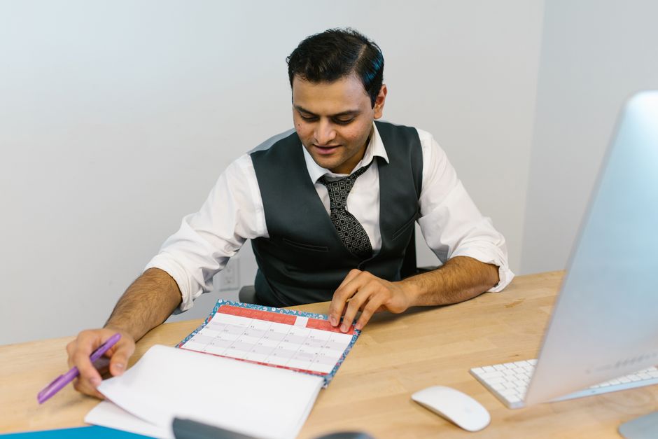 Anxiété du temps : pourquoi chaque minute semble vous échapper A businessman checks his schedule at a desk, referencing a calendar and making notes.