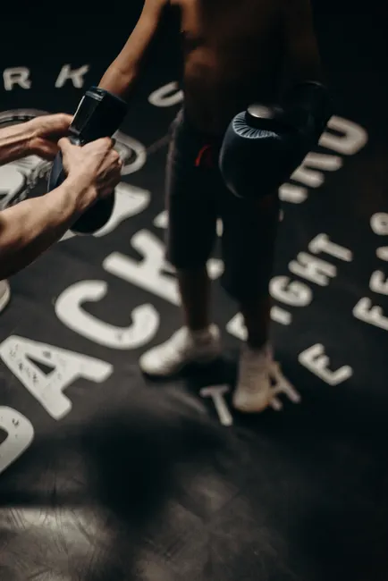 A child boxer receiving guidance from a trainer indoors, focusing on training techniques.