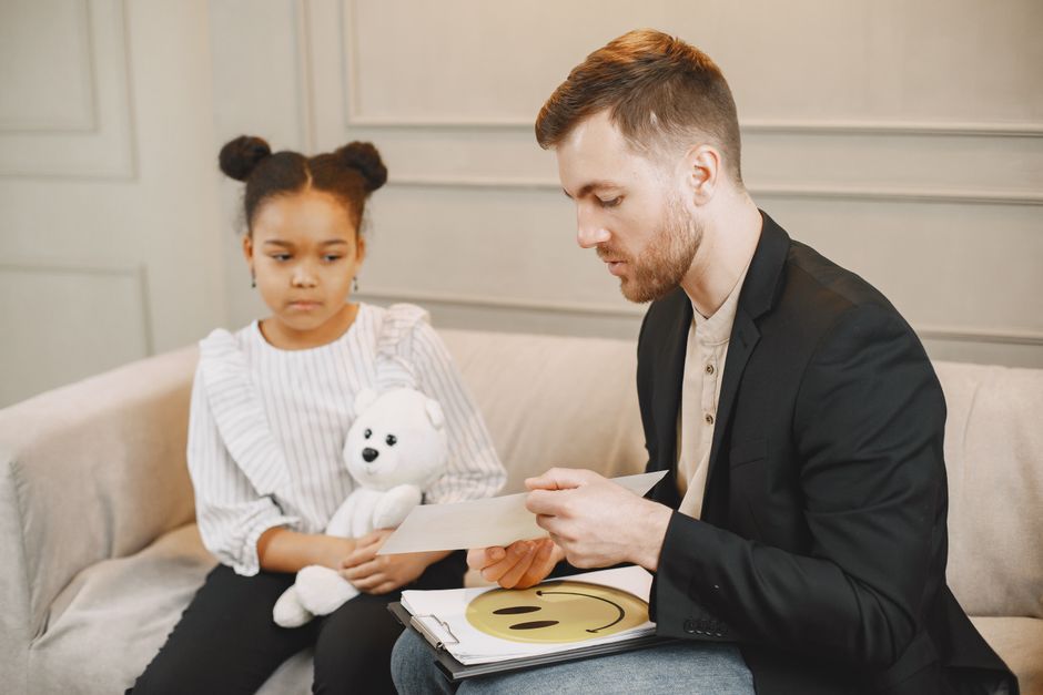 Neurofeedback et TDAH : ce que montrent les études de 2024 et 2025 A child holding a plush toy listens to a man in a therapy session.