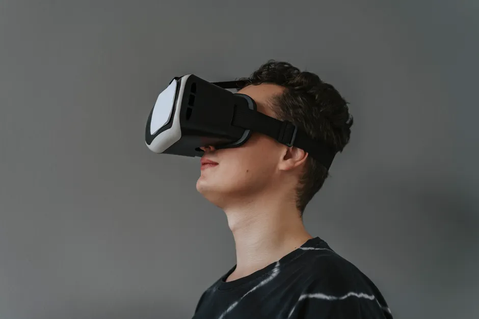 A close-up image of a man wearing a black VR headset against a gray background.