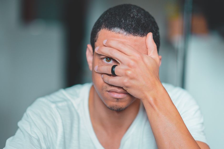 Anxiété sociale en 2026 : ce que les études montrent sur les causes, le cerveau et les interventions numériques A close-up portrait of an adult man with one eye covered by his hand, wearing a black ring.