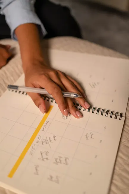 A close-up shot of a hand writing in a planner while resting on a bed.