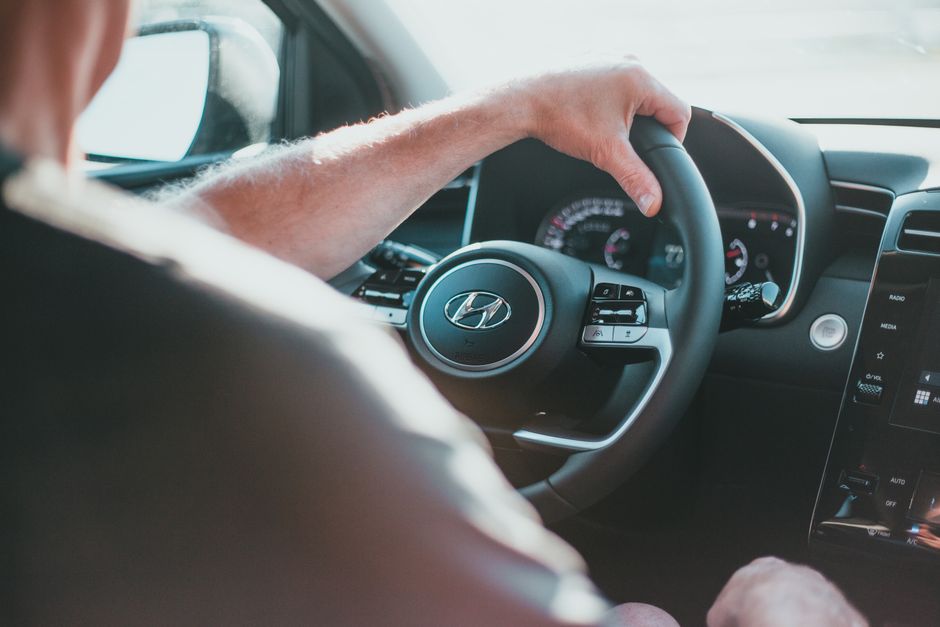 A close-up view of a person's hand gripping a Hyundai steering wheel inside a car.