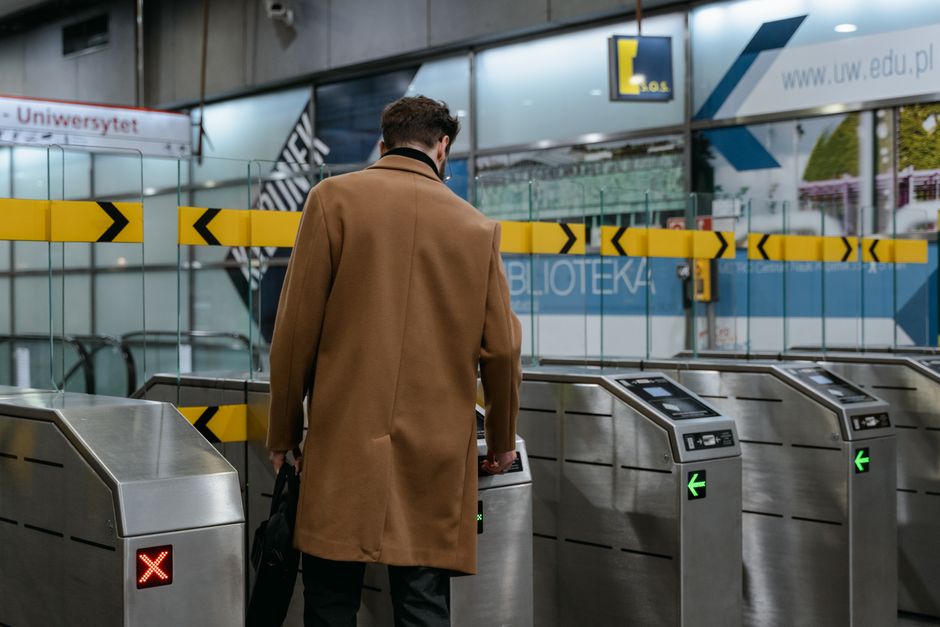 A commuter in a brown coat enters a metro station through ticket barriers.