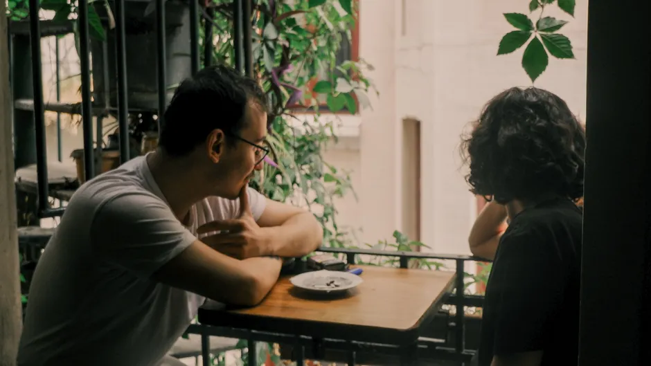 A couple enjoys a relaxed conversation on a leafy urban balcony setting.
