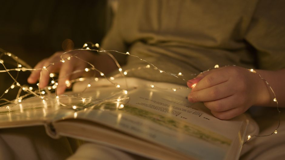 Dyslexie : signes, diagnostic et aides concrètes à tout âge A cozy scene of a child reading a book surrounded by warm, glowing string lights.