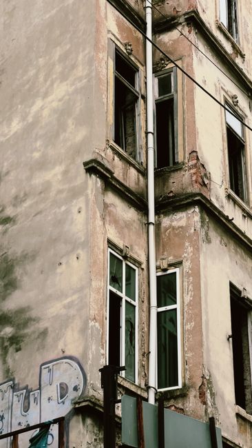 A decaying urban building captured from a low angle, emphasizing its aging architecture and broken windows.