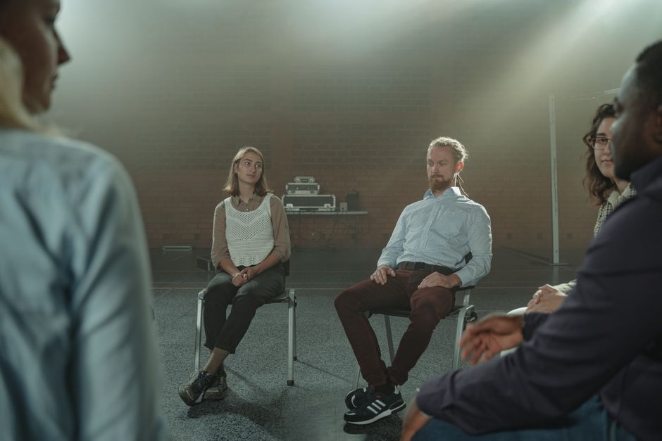 A diverse group of adults engaged in a thoughtful conversation indoors.