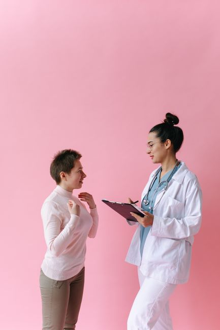A doctor consults with a patient against a pink background, illustrating healthcare professionalism.