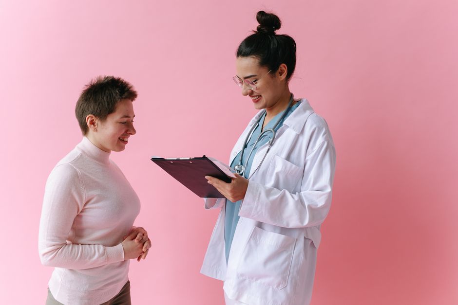 A doctor in a white coat consults a smiling patient against a pink backdrop.